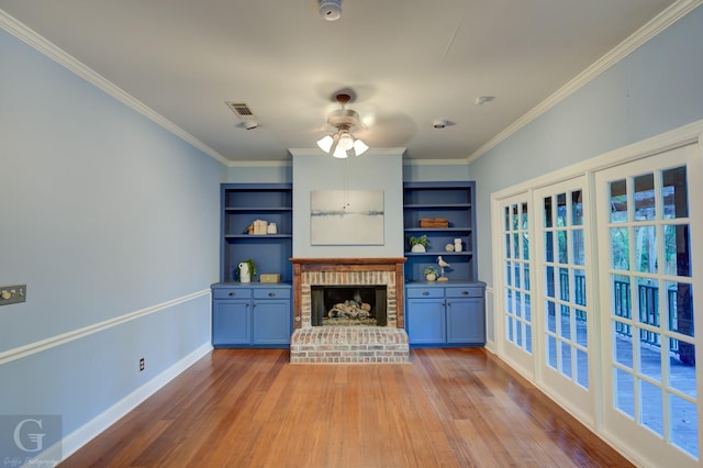 unfurnished living room with built in shelves, crown molding, ceiling fan, and a brick fireplace