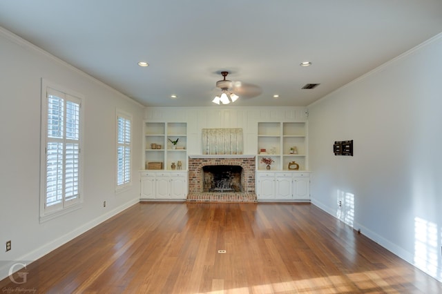 unfurnished living room featuring a brick fireplace, ornamental molding, ceiling fan, built in features, and hardwood / wood-style floors