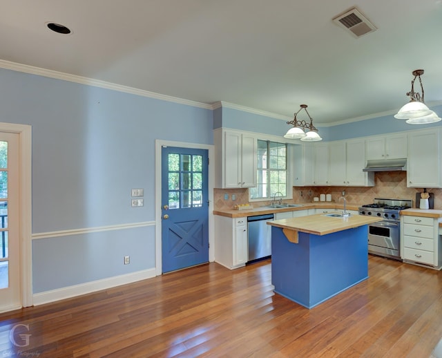 kitchen with appliances with stainless steel finishes, sink, pendant lighting, white cabinets, and a center island