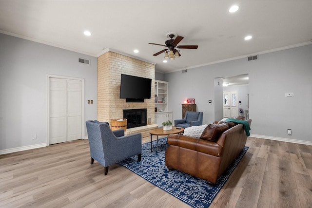 living room with a brick fireplace, ornamental molding, and light wood-type flooring