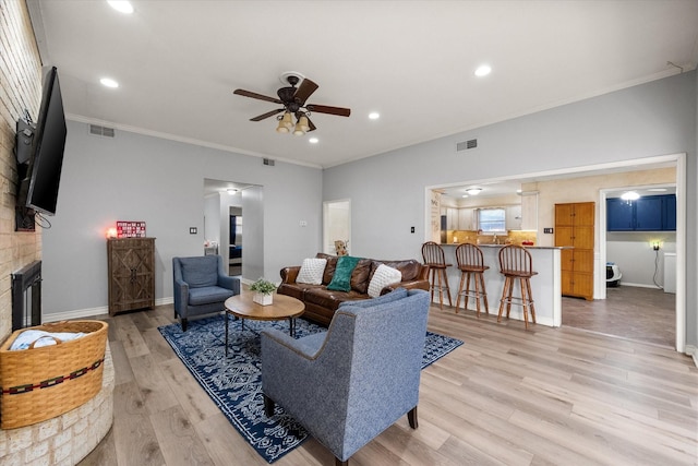 living room featuring crown molding, ceiling fan, a brick fireplace, and light hardwood / wood-style flooring