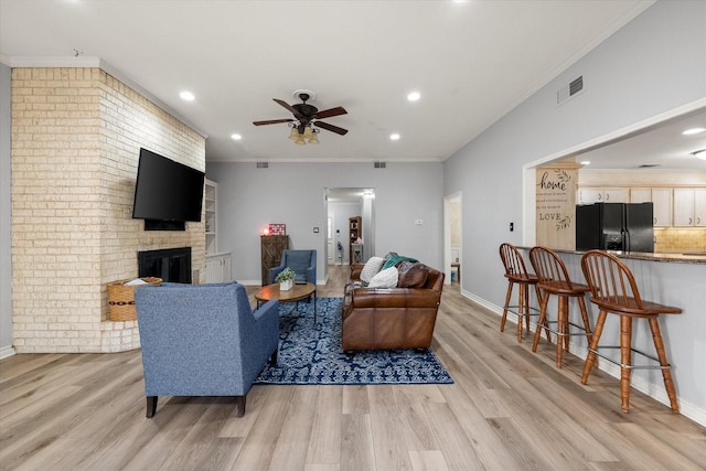 living room featuring a brick fireplace, light hardwood / wood-style flooring, ornamental molding, and ceiling fan