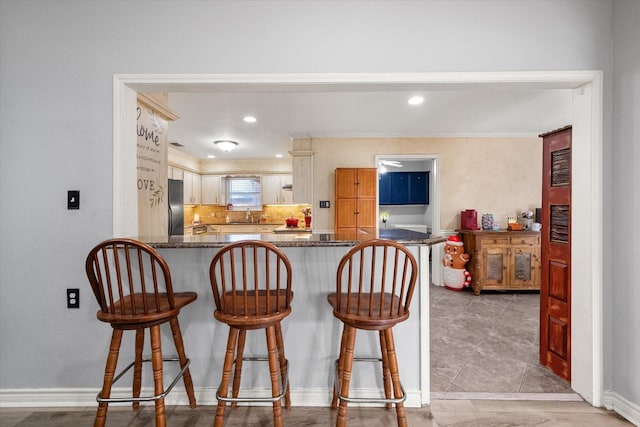 kitchen with black refrigerator, a kitchen breakfast bar, kitchen peninsula, and dark stone countertops