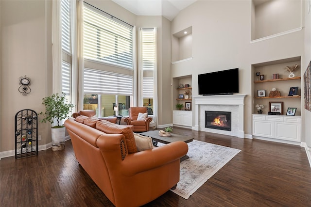 living room with built in shelves, a towering ceiling, and dark hardwood / wood-style flooring