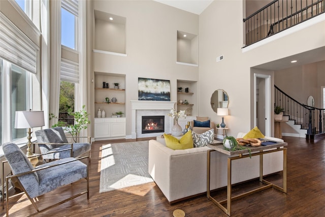 living area with a high ceiling, built in features, a glass covered fireplace, stairs, and visible vents