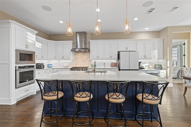 kitchen with stainless steel oven, wall chimney range hood, hanging light fixtures, white fridge, and white cabinetry