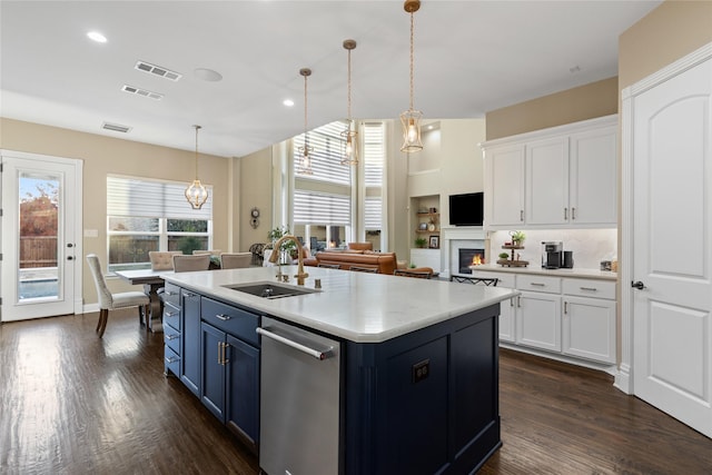 kitchen featuring a center island with sink, sink, hanging light fixtures, blue cabinetry, and white cabinetry