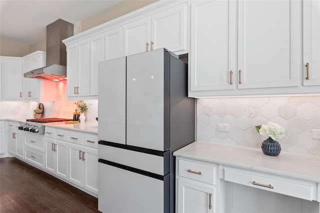 kitchen with wall chimney range hood, tasteful backsplash, white cabinets, and freestanding refrigerator
