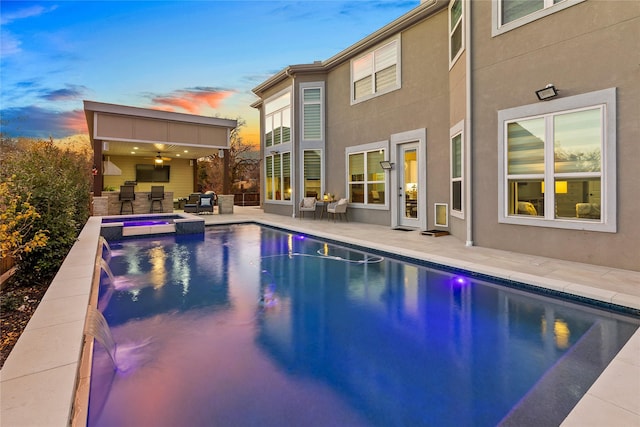 rear view of house with stucco siding, a patio area, and a pool with connected hot tub