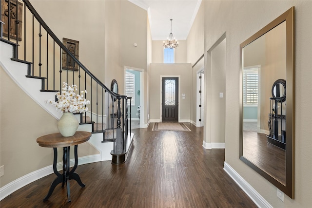 entrance foyer with a notable chandelier, ornamental molding, dark wood-type flooring, and a high ceiling