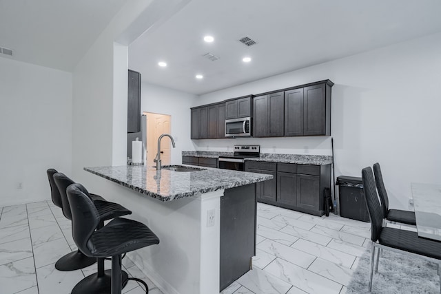 kitchen with stone counters, sink, stainless steel appliances, kitchen peninsula, and dark brown cabinets