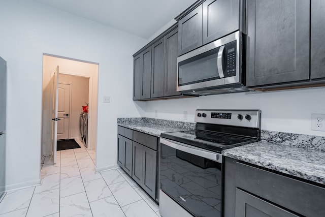 kitchen with washer / dryer, light stone countertops, and stainless steel appliances