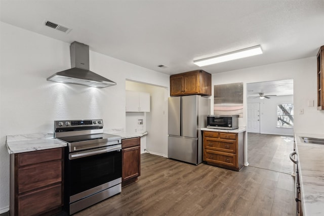 kitchen with wall chimney exhaust hood, dark hardwood / wood-style floors, ceiling fan, light stone countertops, and stainless steel appliances