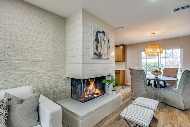 living room featuring light wood-type flooring, a brick fireplace, and a notable chandelier