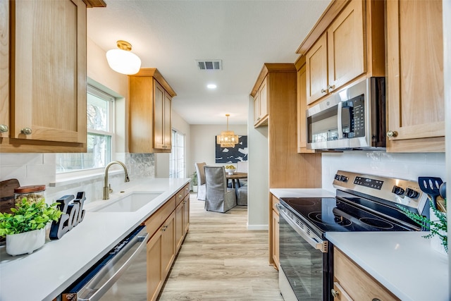 kitchen featuring sink, light wood-type flooring, appliances with stainless steel finishes, tasteful backsplash, and decorative light fixtures