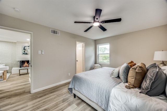 bedroom featuring ceiling fan, light wood-type flooring, and a fireplace