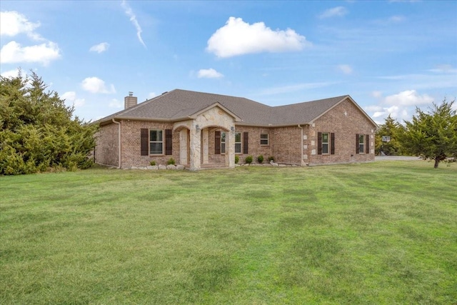 french country home featuring a shingled roof, a front yard, brick siding, and a chimney