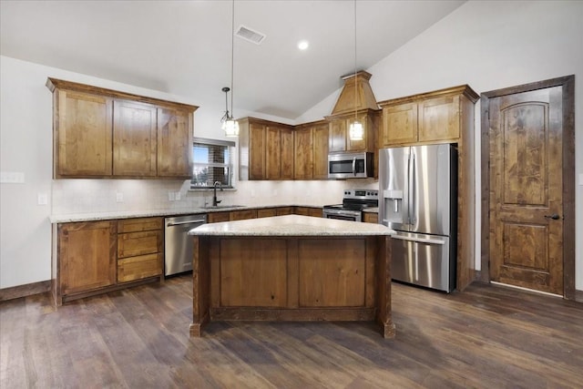 kitchen with appliances with stainless steel finishes, dark wood-type flooring, sink, decorative light fixtures, and a kitchen island