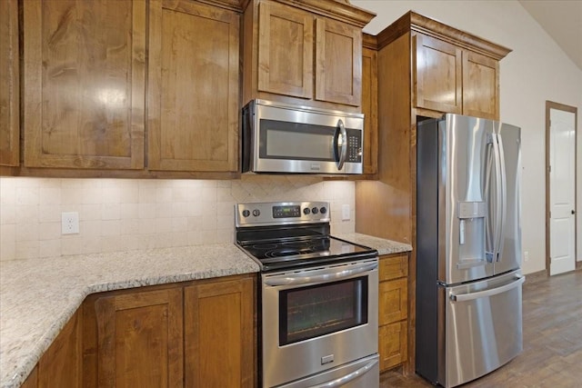 kitchen with brown cabinetry, dark wood finished floors, stainless steel appliances, and decorative backsplash