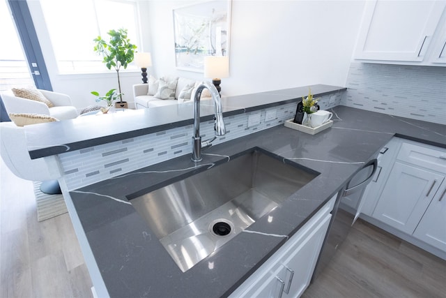 kitchen with tasteful backsplash, white cabinetry, wood-type flooring, and sink