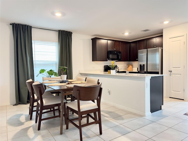 kitchen with kitchen peninsula, stainless steel fridge, dark brown cabinets, and light tile patterned flooring