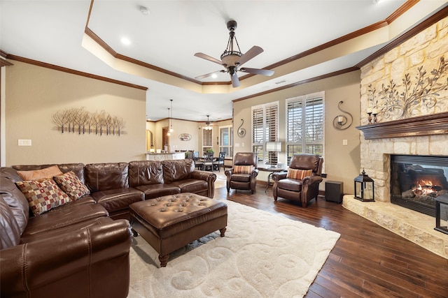 living room featuring ceiling fan, a stone fireplace, crown molding, hardwood / wood-style floors, and a tray ceiling