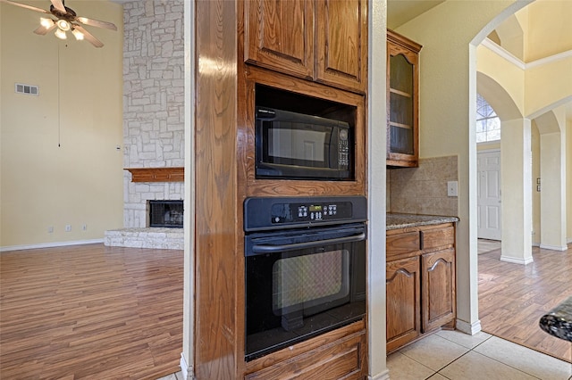 kitchen featuring ceiling fan, a stone fireplace, light hardwood / wood-style flooring, backsplash, and black appliances