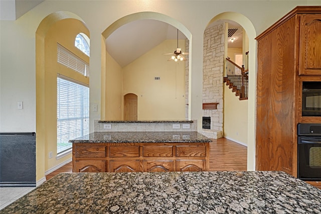 kitchen with vaulted ceiling, oven, ceiling fan, and dark stone countertops