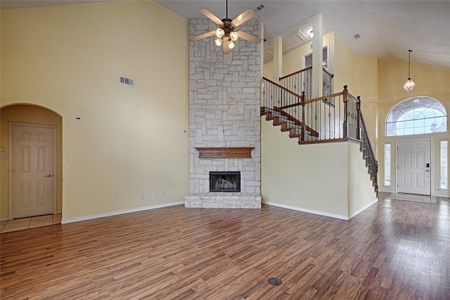 unfurnished living room with a stone fireplace, ceiling fan, hardwood / wood-style floors, and high vaulted ceiling