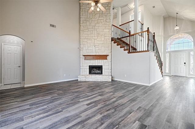 unfurnished living room featuring ceiling fan, dark hardwood / wood-style floors, high vaulted ceiling, and a stone fireplace