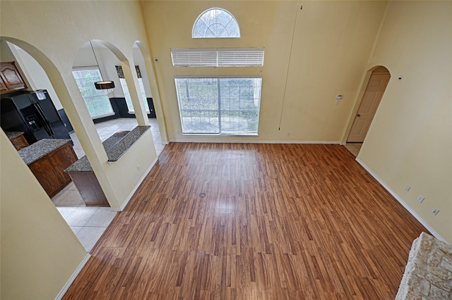 unfurnished living room featuring a healthy amount of sunlight, light hardwood / wood-style floors, a fireplace, and a towering ceiling