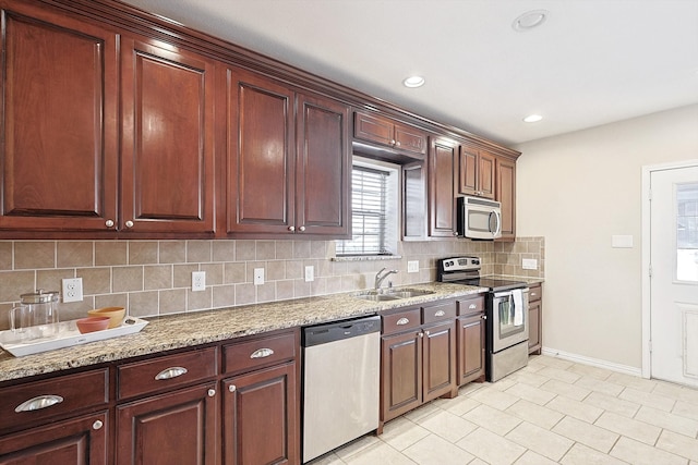 kitchen with backsplash, light stone counters, sink, and appliances with stainless steel finishes