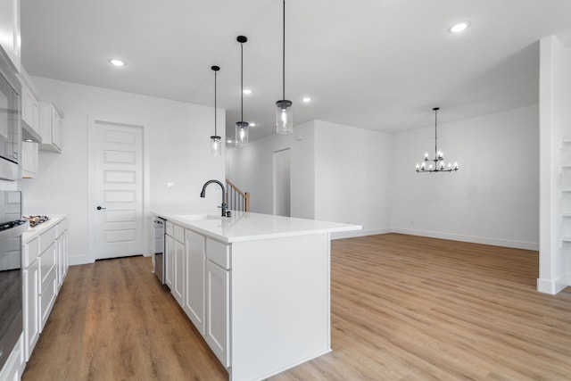 kitchen featuring white cabinetry, sink, light hardwood / wood-style flooring, decorative light fixtures, and a kitchen island with sink