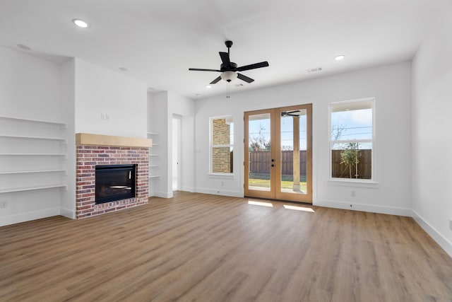 unfurnished living room with french doors, light hardwood / wood-style flooring, ceiling fan, built in shelves, and a fireplace