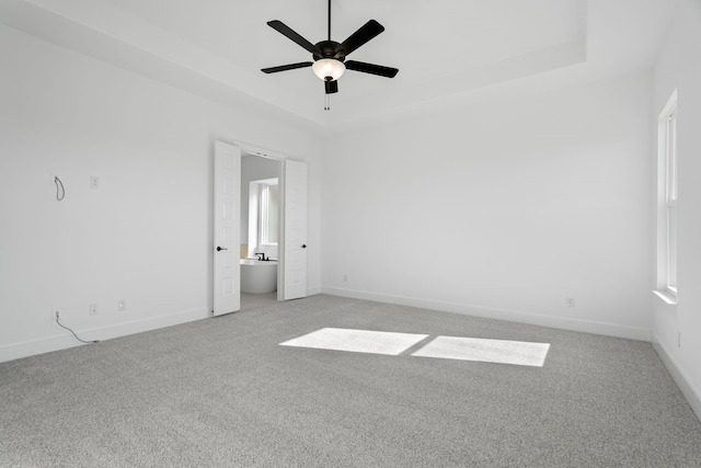 spare room featuring a raised ceiling, ceiling fan, and light carpet