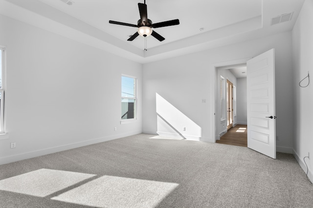 carpeted spare room featuring a tray ceiling and ceiling fan