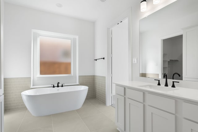 bathroom with tile patterned flooring, vanity, a bath, and tile walls