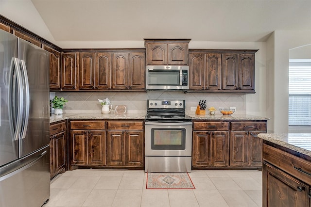 kitchen featuring appliances with stainless steel finishes, tasteful backsplash, light stone counters, dark brown cabinets, and vaulted ceiling