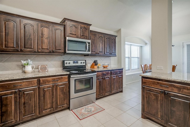 kitchen featuring tasteful backsplash, light stone counters, dark brown cabinets, and stainless steel appliances