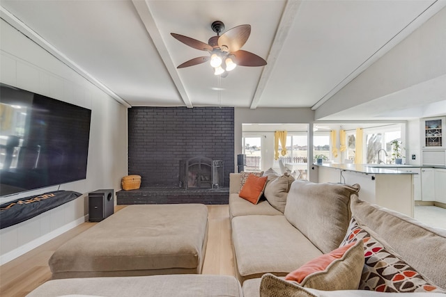 living room with hardwood / wood-style floors, a fireplace, beamed ceiling, sink, and ceiling fan