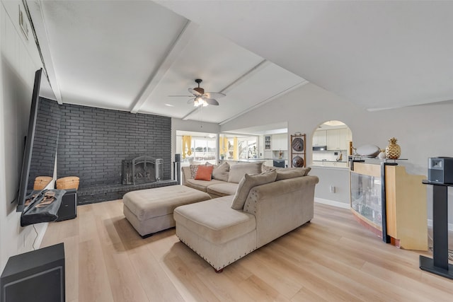 living room with ceiling fan, a fireplace, light hardwood / wood-style floors, lofted ceiling with beams, and brick wall