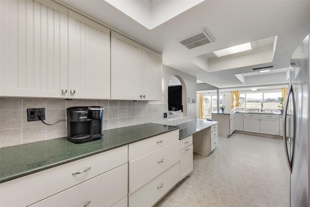 kitchen featuring tasteful backsplash, a raised ceiling, stainless steel refrigerator, and white cabinets