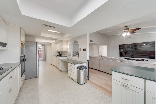 kitchen with tasteful backsplash, white cabinetry, ceiling fan, black appliances, and a raised ceiling