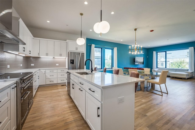 kitchen with sink, hanging light fixtures, wall chimney range hood, a center island with sink, and white cabinets