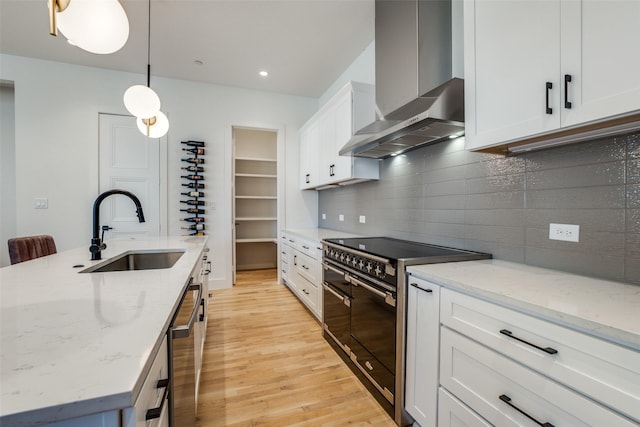 kitchen featuring white cabinets, double oven range, wall chimney exhaust hood, and sink