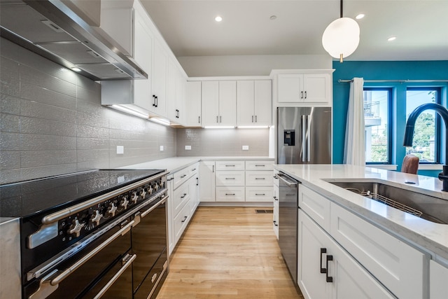 kitchen featuring light stone countertops, white cabinetry, sink, stainless steel appliances, and wall chimney range hood