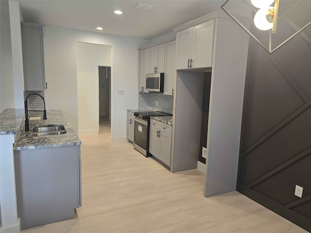 kitchen with backsplash, stainless steel appliances, light stone counters, and sink