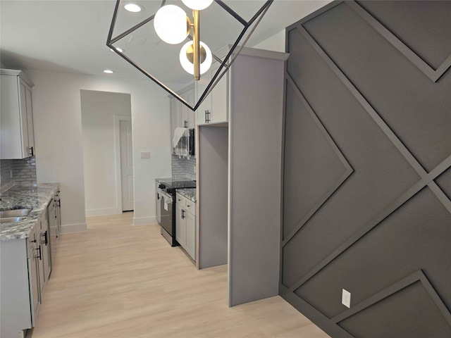 kitchen with light stone counters, backsplash, pendant lighting, appliances with stainless steel finishes, and light wood-type flooring