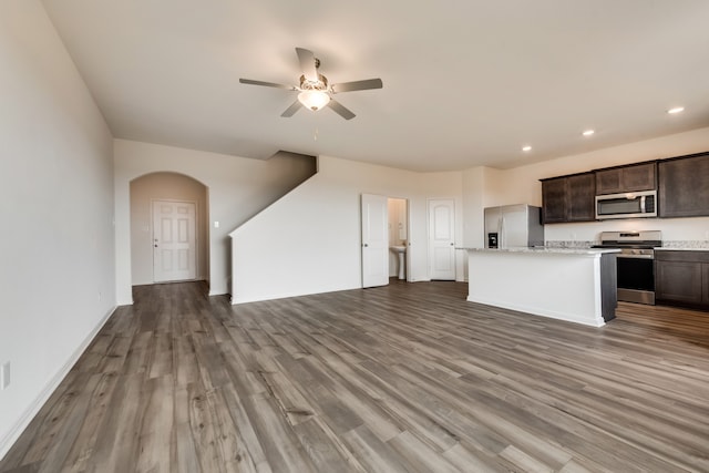 kitchen with appliances with stainless steel finishes, dark brown cabinets, ceiling fan, hardwood / wood-style floors, and a center island