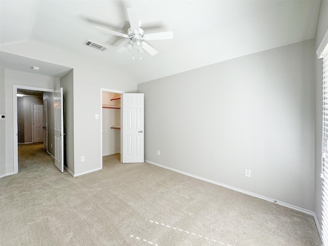 unfurnished bedroom featuring lofted ceiling, a walk in closet, light carpet, a closet, and ceiling fan